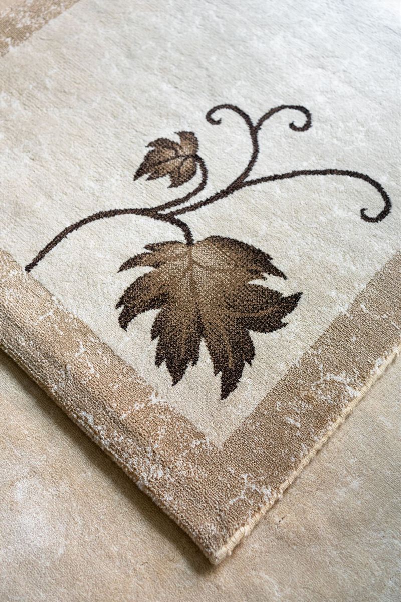 Close-up corner of a folded, elegant cream area rug with a woven brown leaf motif.